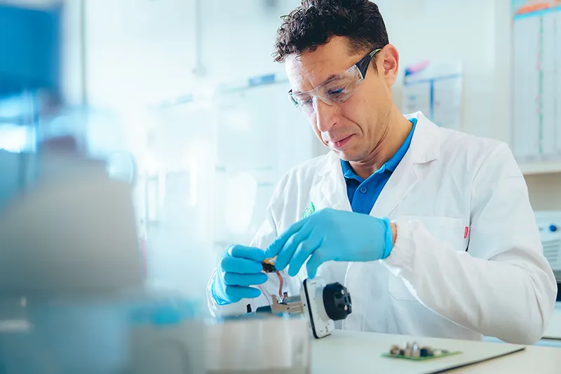 Technicien concentré sur l’assemblage d’un dispositif technique de précision, illustrant le savoir-faire industriel et scientifique