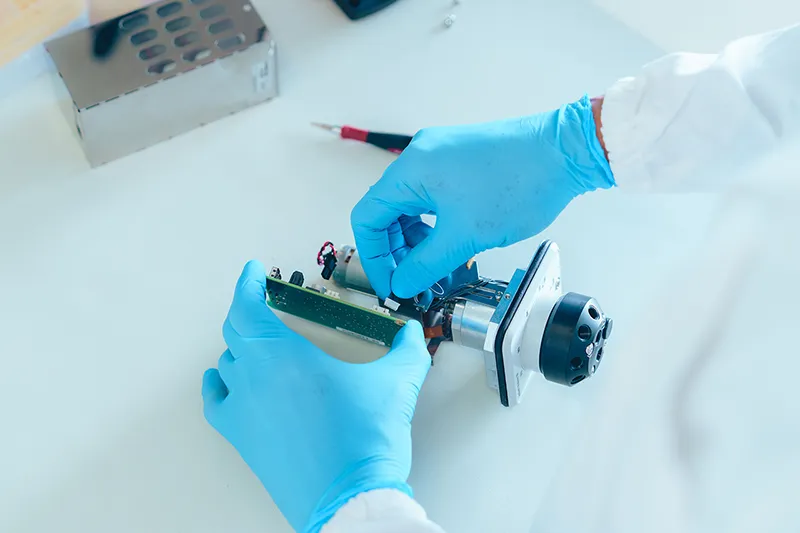 Gros plan sur la réparation d’un composant électronique de précision en laboratoire, illustrant les compétences techniques AKTA en Suisse
